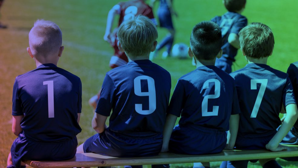 Children sitting on the sidelines of a sports event
